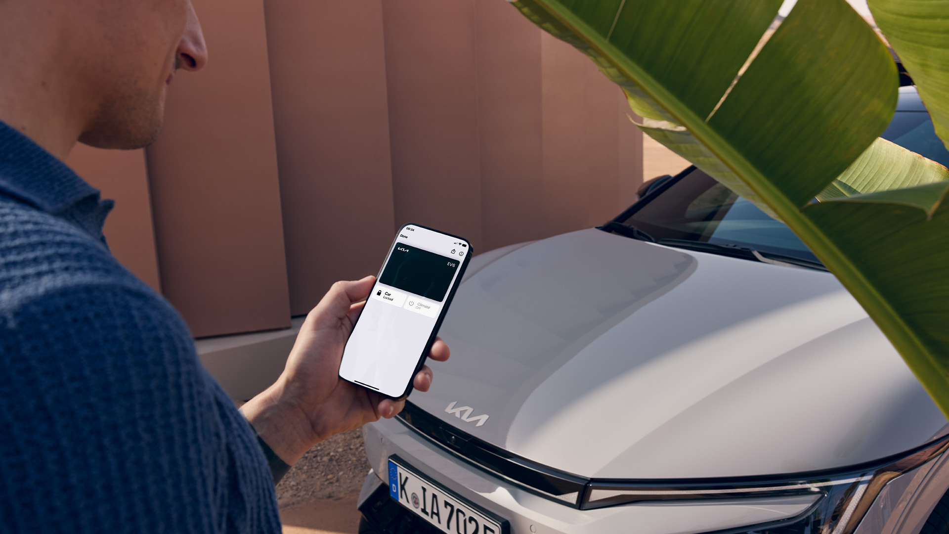 Kia EV6 steht in Einfahrt, Smartphone mit Fahrzeug.Infos auf Display