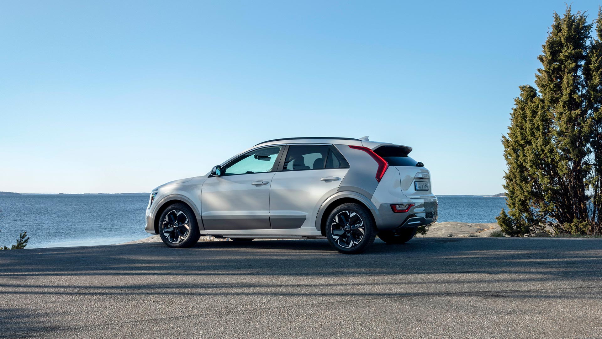 Nya Kia Niro EV står parkerad på en strand vid vattnet, solen skiner.