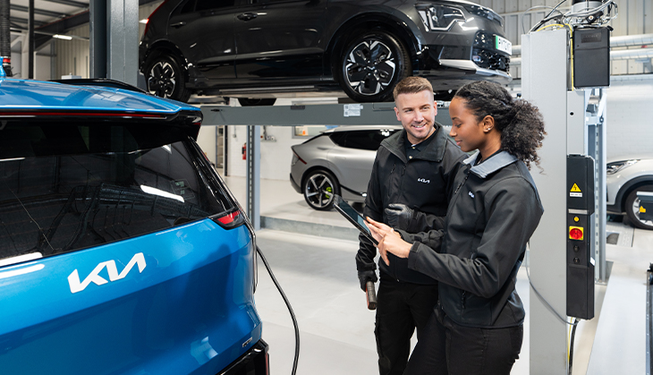 Two technicians standing beside a Kia EV9 car in a garage.